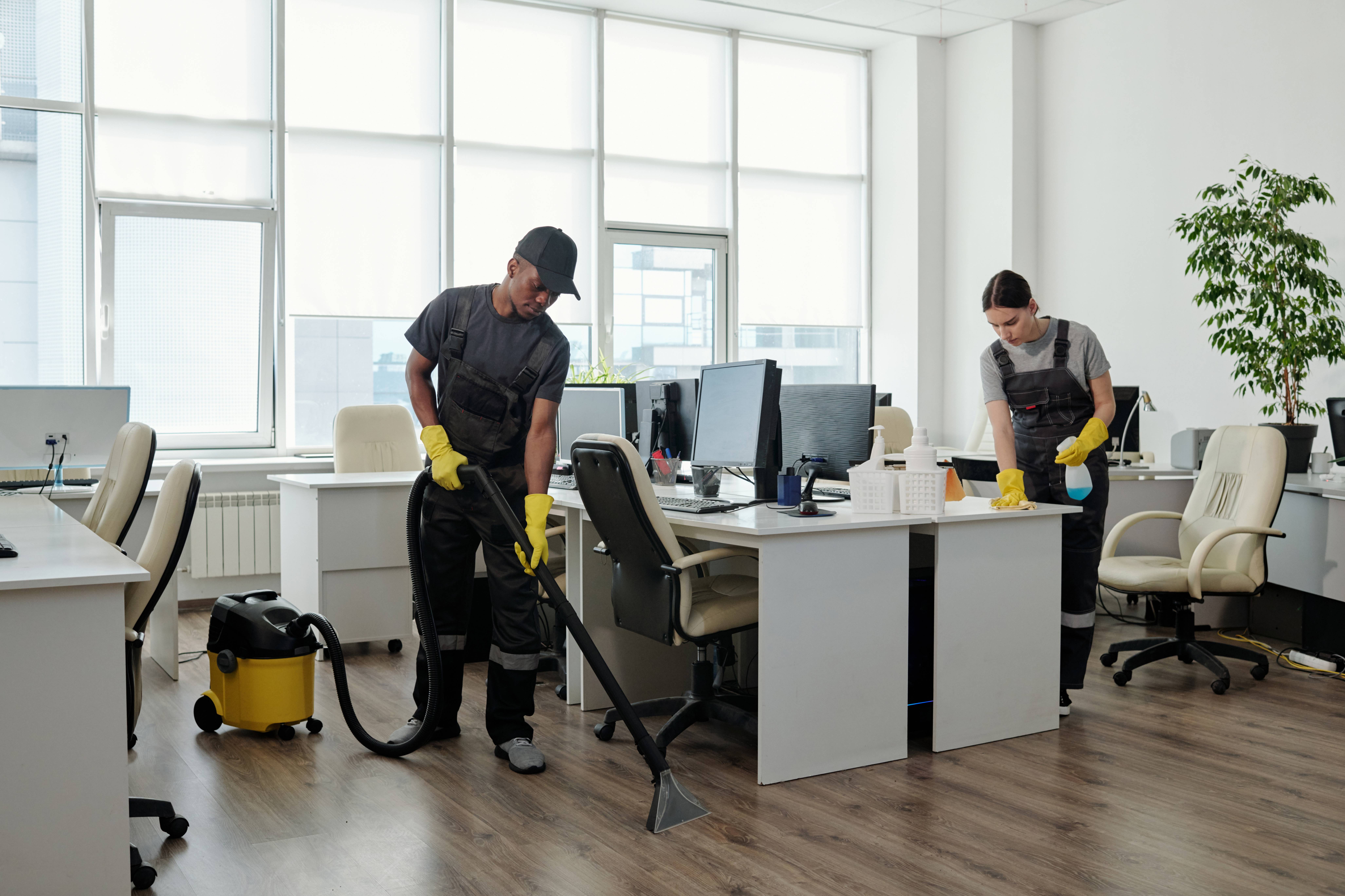 young-black-man-workwear-cleaning-floor-while-girl-wiping-desks-with-computers